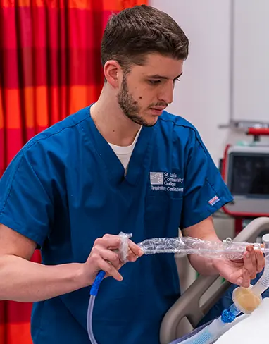 A medical student wearing scrubs, working on a dummy