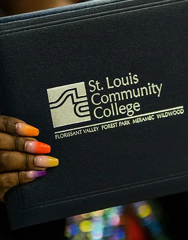 A well-manicured hand holding their STLCC diploma