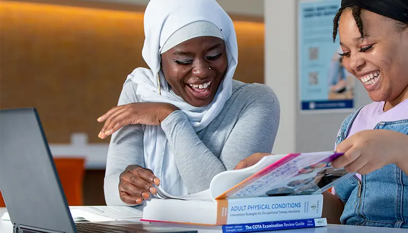 Two students excitedly reading an Adult Physical Conditions textbook