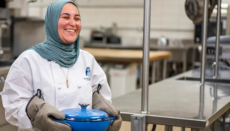 A culinary student proudly holding a covered dish they have prepared